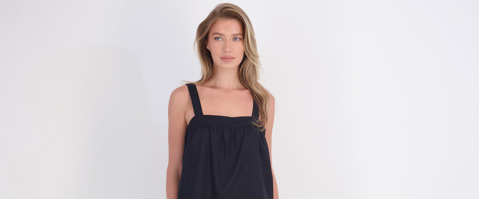 model wearing dark blue cotton sleeveless top on grey background feeling confident