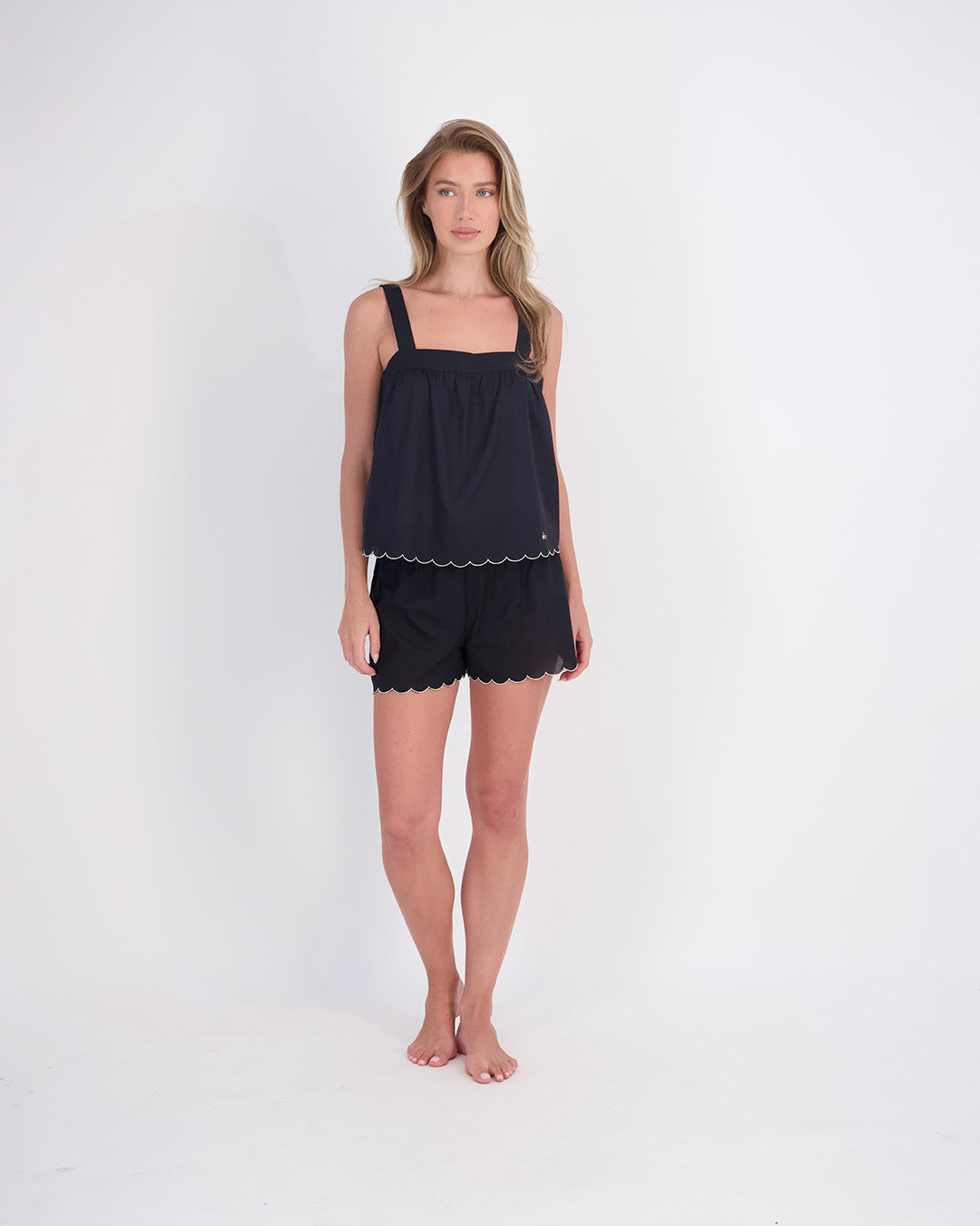 model wearing black sleeveless top and matching shorts on grey background feeling confident
